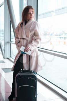 Passenger woman in airport waiting for air travel. Young business woman standing with travel suitcase in waiting hall of departure lounge in airport