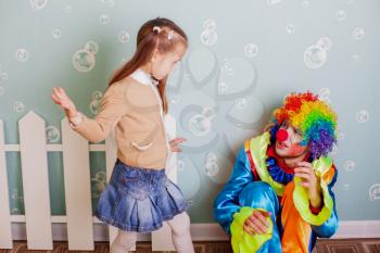 During the game a little girl hits upset clown. Decoration room on the background.