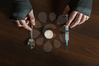 Hands with spoon and heroin syringe closeup, wooden background.