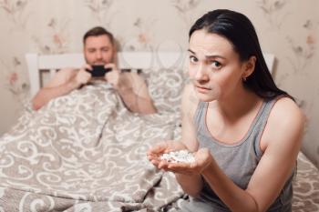 Wife trying to eat a lot of tablets while husband use his phone in bed. Family life problems