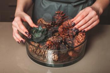 Florist creating christmas decoration closeup. Dry pine cones in glass bowl.