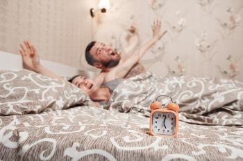  Young couple wakeup in the bed in the morning. Alarm clock on the bed against young couple.