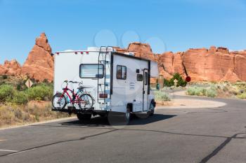 Camper with bikes on asphalt road. Rocky mountains on the background.