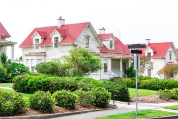 Gently slanted lawn in front of white cozy house. Estate exterior architecture.