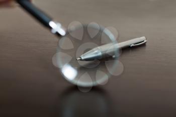 Looking on a pen through magnifying glass, wooden background