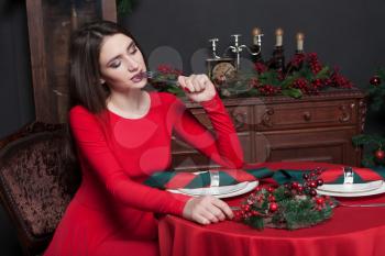 Beauty girl in red dress sitting at the table in restaurant with rich interior.