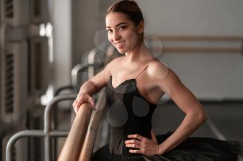 Female ballet dancer hold on to the barre in class. Beautiful smiling ballerina on dance rehearsal 