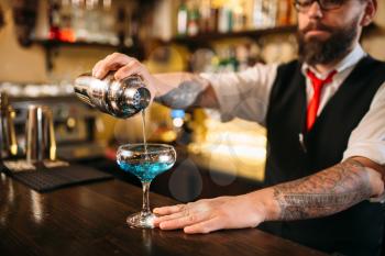 Bartender with shaker making alcohol cocktail behind a bar counter