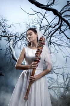 Beautiful bride with bloody baseball bat against the background of the dried tree