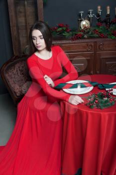 Young woman waiting in vintage restaurant. Glamour female in red dress, romantic evening.