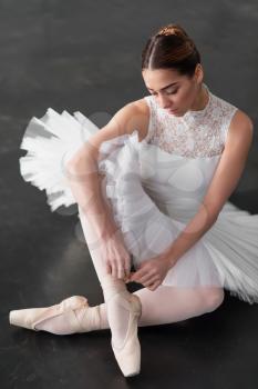 Beautiful ballerina posing in ballet class, barre and white wall on background
