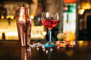 Beverage in glass, shaker, lime, lemon, salt and dice on wooden bar counter