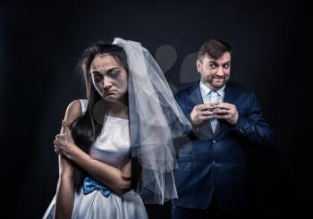 Bride with tearful face, groom with sly smile on background. Unhappy marriage