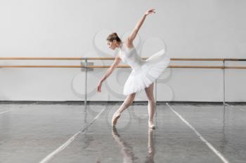Beautiful ballerina rehearsal in ballet class, barre and white wall on background