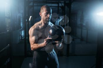 Strong weightlifter workout with kettlebell in gym. Man with muscular torso training with weight