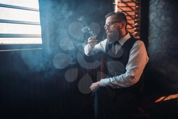 Portrait of bearded man in glasses sitting on a chair and smoking pipe. Writer, journalist, literature author, blogger or poet concept