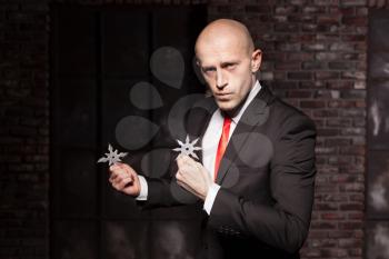 Professional secret agent explore oriental martial arts concept. Bald contract murderer in suit and red tie holds asterisk ninja. Chouraqui dangerous weapon in right hands
