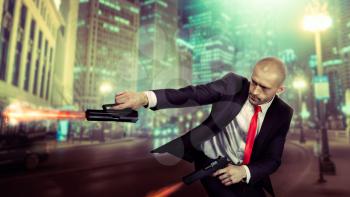 Bald assassin in suit and red tie shoot a pistols with two hands, night urban landscape on background. Contract killer shooting action wallpaper or poster concept