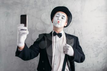 Pantomime actor with makeup mask makes selfie on camera. Comedy artist in suit, gloves and hat