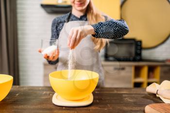 Female person adds sugar into a bowl, cake cooking on wooden table. Fresh tasty dough preparation