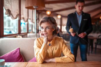 Beautiful woman waiting in restaurant, man with rose in hand on background