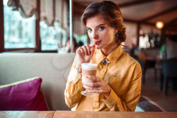 Attractive woman drinks a cocktail from the straw, restaurant on background