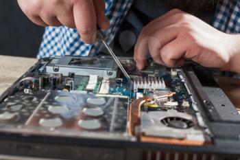 Male engineer hands repairs laptop with screwdriver closeup view. Electronic devices repairing technology