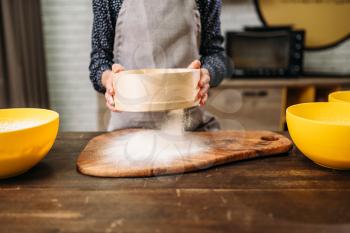 Female person filters the flour through a sieve on wooden table. Cake cooking. Dough preparation