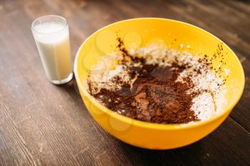 Bowl with dough, chocolate powder and glass of milk on wooden background. Sweet cake cooking. Homemade dessert ingredients
