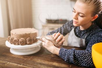 Woman cook decorate chocolate cake with culinary syringe. Kitchen on background. Homemade dessert decoration