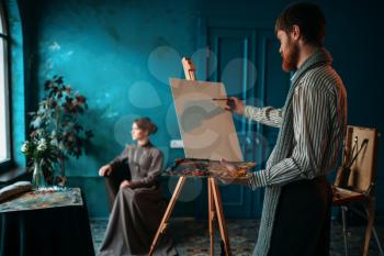Male artist with palette and brush in hand in front of easel. Oil paint