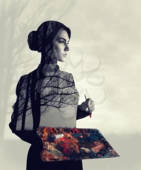 Female painter with brush and palette in hands, body with forest texture, double exposure. Woman on blur background