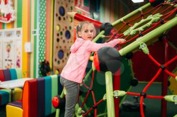 Little girl climbing on a ropes on playground in childrens entertainment center. Child sport activity. Happy childhood