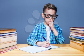 Little child writing in notebook and picks his nose, school homework concept. Young pupil at the desk in classroom
