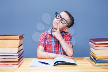 Young boy dreams at the desk in school library. Schoolboy in glasses against many books. Little pupil concept