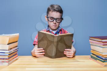 Scientist little child in glasses reading a book in the school library. Education concept