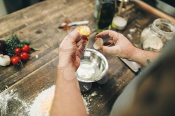 Homemade pasta cooking process, dough preparation. Male chef hands with egg, a bunch of flour on wooden table