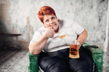 Overweight woman sitting in chair and drinks beer, bulimic, obesity. Unhealthy lifestyle, fatty female