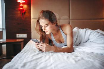 Attractive woman lies in bed and using phone. Girl wake up in the morning in bedroom