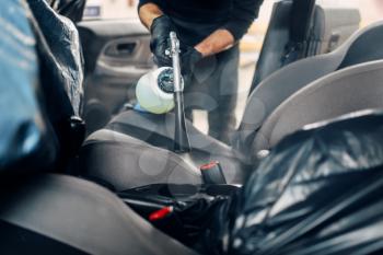 Professional dry cleaning of car seats. Carwash service, male worker in gloves using spray