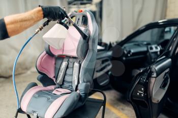 Carwash service, worker in gloves removing dust and dirt from child seat. Professional dry cleaning of car interior with vacuum cleaner