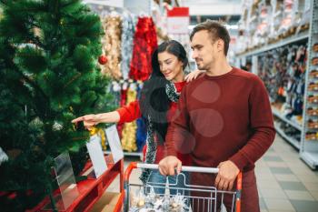 Couple buying new year goods in supermarket. Christmas shopping, choosing of holiday decorations