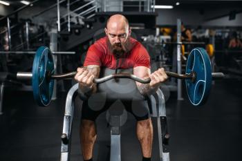 Muscular athlete doing exercise with barbell in gym. Bearded man on workout in sport club, healthy lifestyle