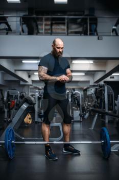 Muscular athlete in sportswear prepares to takes weight, training in gym. Bearded man on workout in sport club, healthy lifestyle