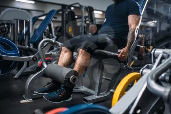 Muscular male person trains legs on exercise machine, training in gym. Bearded man on workout in sport club, healthy lifestyle