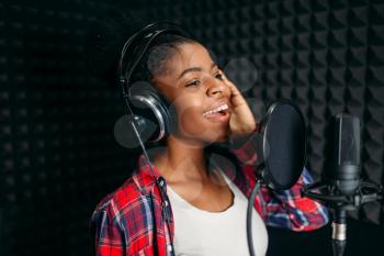 Female singer in headphones songs in audio recording studio. Musician listens composition, professional music mixing