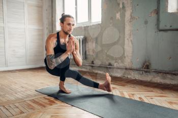 Male yoga in class, balance training. Exercise on mat in gym with grunge interior. Fit workout indoors