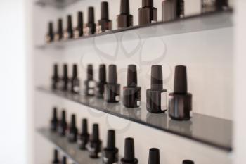 Rows of black nameless nail varnish bottles on the shelf in beauty shop. Professional manicure and pedicure accessory, nobody. Beautician salon, cosmetology studio, unnamed enamel containers
