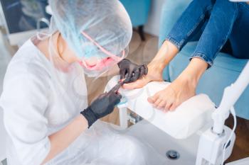 Beautician salon, pedicure, cuticle removal procedure. Nail care treatment for female client in beauty shop, doctor in gloves works with customer toenails