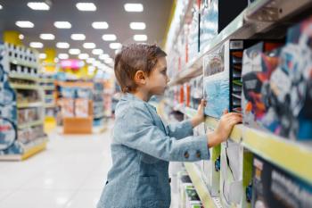 Little boy at the shelf in kids store, side view. Son choosing toys in supermarket, family shopping, young customer buying model